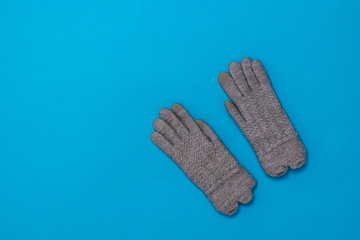 A pair of grey knitted gloves for women on a blue background.
