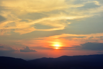 sunset sunrise in orange colors and sun over dark mountain silhouette.
