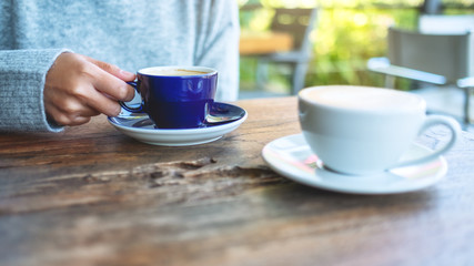 Closeup image of a woman holding and drinking hot coffee in the outdoors