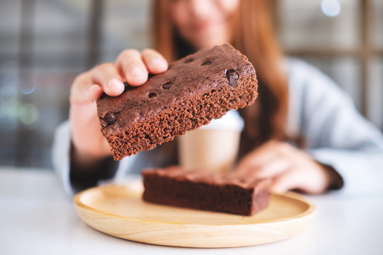 Closeup image of a beautiful woman holding and showing a piece of brownie cake