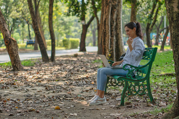 young caacasian university student or businesswoman sitting under tree in natural park using laptop computer for work