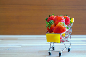 Close up strawberry on shopping cart with white and brown wooden background,text advertising, diet...