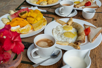 Tropical breakfast of fruit, coffee and scrambled eggs and banana pancake for two on the beach near sea