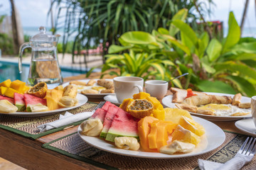 Tropical breakfast of fruit, coffee and scrambled eggs and banana pancake for two on the beach near sea