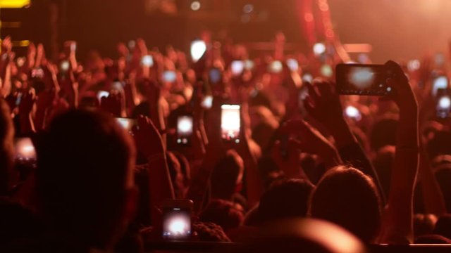 Energetic people dancing with their hands up at the punk concert - some people filming the performance on the phone cameras