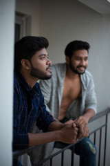 Two young tall, dark and handsome Indian Bengali men in western jackets and shirt spending time together standing on balcony in white background. Indian lifestyle.
