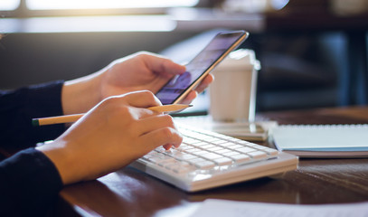 Closeup of hand businesswoman using computer and mobile phone working on desk