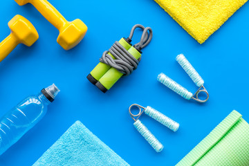 Fitness background - dumbbells, jump rope, sport carpet, water bottle - on blue top-down pattern