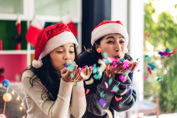 Cute girl and mother in santa hats having fun blowing glitter and smiling while celebrating new year eve and enjoying spending time together in christmas time at home
