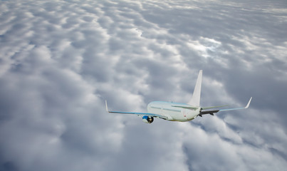 White passenger plane flying over grey clouds.