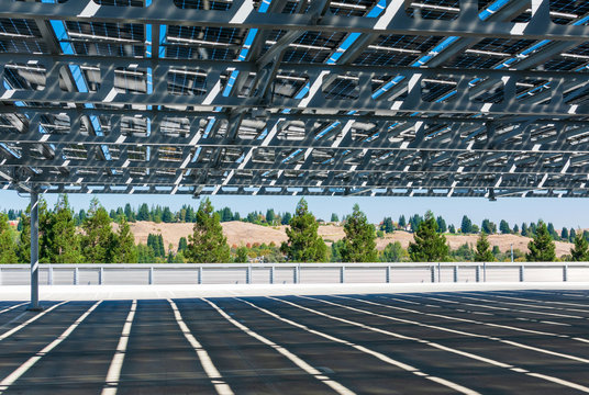 Solar panels installed as solar canopy on top of parking garage. Solar power panels convert sunlight into clean electricity, renewable energy and provide shade for cars. Green trees background. 