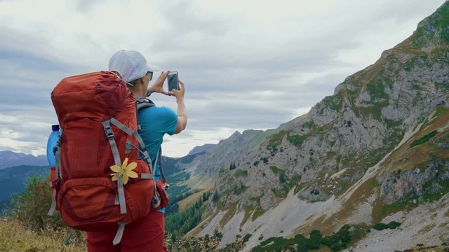 Young tourist backpacker woman taking a panorama photo of the mountains with her phone, wide shot
