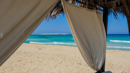 Fototapeta na wymiar Marsa Matruh, Egypt. The sandy beach and the amazing sea with tropical blue, turquoise and green colors. View through a gazebo. Relaxing context. Fabulous holidays. Mediterranean Sea