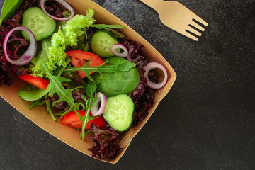 Healthy salad, leaves mix salad in paper disposable tableware (mix micro greens, cucumber, tomato, onion, other ingredients). food background. copy space