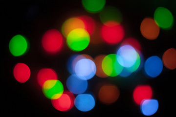 Abstract unfocused background - colorful bokeh of different bubbles on a black background. Modern blurred pattern for design and for Christmas, New year and funny holiday backdrops..