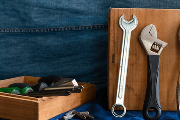 Hand tools such as hammers, pliers, wrenches, screwdrivers, many types of screwdrivers and other tools that are in a wooden box placed on a blue denim background.