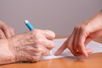 Woman of retirement age signs a document. Elderly woman signs a paper document. Signing papers. An...