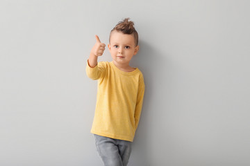 Portrait of cute little boy showing thumb-up on light background