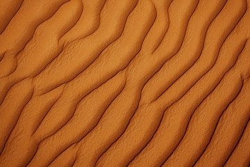 Naklejka na ściany i meble Wavy sandy texture on the dunes in the desert close-up. View from above