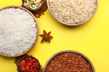 Plates with different raw rice, vegetables and spices on color background