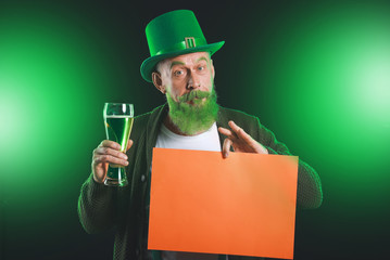 Funny mature man with blank poster and glass of beer on dark background. St. Patrick's Day...