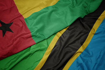 waving colorful flag of tanzania and national flag of guinea bissau.