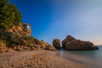 Sandy beach on the Spanish coast of the Costa del Sol. Viewpoint Balcon Europa in Nerja on sunny day as a view over the Mediterranean. View of rocks with palm trees and rocks on the beach