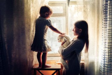 cozy sisters children gently play with cat, window