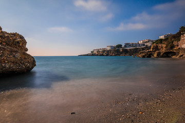 Fototapeta na wymiar Beach section on the Mediterranean coast in Nerja. Sandy beach on the Spanish coastline of Costa del Sol with rocks on sunny day with blue sky and clouds