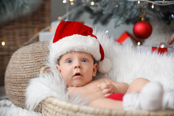 Fototapeta na wymiar Cute little baby with Santa Claus hat lying in basket at home