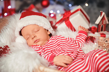Cute little baby with Santa Claus hat and Christmas gift sleeping in basket at home
