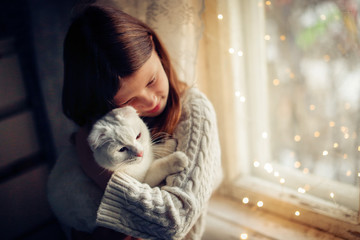 Caucasian kid girl in knitted dress holding cat