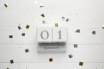 Calendar with date of New Year and confetti on wooden background