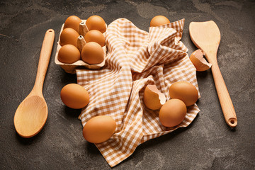 Package with fresh eggs and spoon on dark background