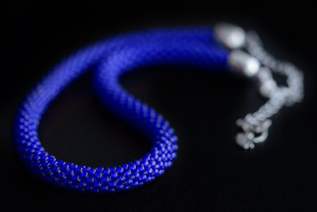 Bead crochet necklace blue color a dark surfce close up. Fashion background