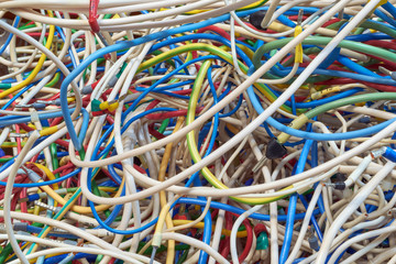 The bunch of electric wires of different colors are very much intertwined. On tangled wires is wire-end ferrules and markings. Chaos, confusion, tangle. Abstract background.