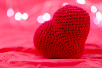 Valentine's day background. Big red knitted heart on a red background with garland lights. Side view, close-up.