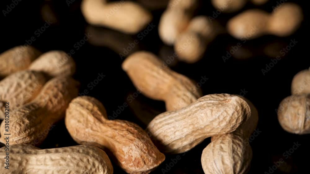 Poster closeup of peanuts in shell fall on black table. static studio shot.
