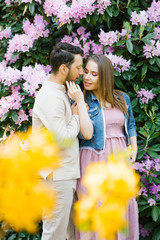 Fototapeta premium A loving couple kissing in the flowering gardens of rhododendron. Tenderness and love in a relationship. Valentine's day