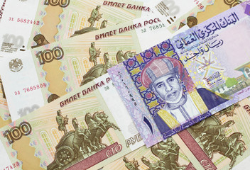 A close up image of a colorful one rial bank note from Oman on a bed of Russian one hundred ruble bank notes in macro