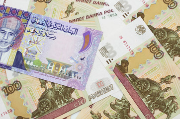 A close up image of a colorful one rial bank note from Oman on a bed of Russian one hundred ruble bank notes in macro