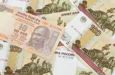 A close up image of an orange ten Indian rupee bank note in macro on a bed of Russian one hundred ruble bank notes