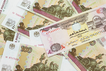 A close up image of a five dirham bank note from the United Arab Emirates on a background of Russian one hundred ruble bank notes in macro