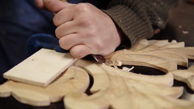 Carpenter working on a wooden in his workshop on the table, preparing a detail of wooden product, a part of future furniture. Close up footage of a man's hands cuts out patterns with a planer