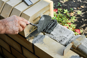 Bricklayer installing bricks on the new fence from facing bricks using putty knife.