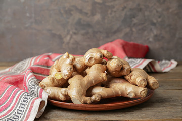 Plate with fresh ginger on wooden table