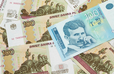 A close up of a blue and white, one hundred Serbian dinar bank note on a background of Russian one hundred ruble bank notes