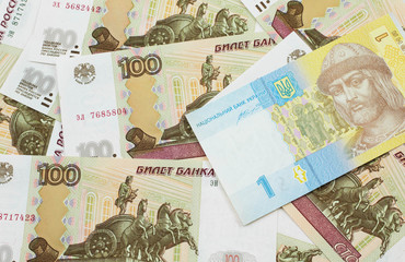 A blue and yellow one Ukrainian hryvnia bank note on a bed of Russian one hundred ruble bank notes