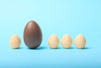 Brown chocolate Easter egg among white ones on color background. Concept of uniqueness