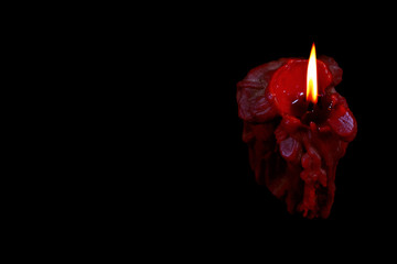 Single red burning candle on black. Copy space. Candle has been burning for a long time and melted....
